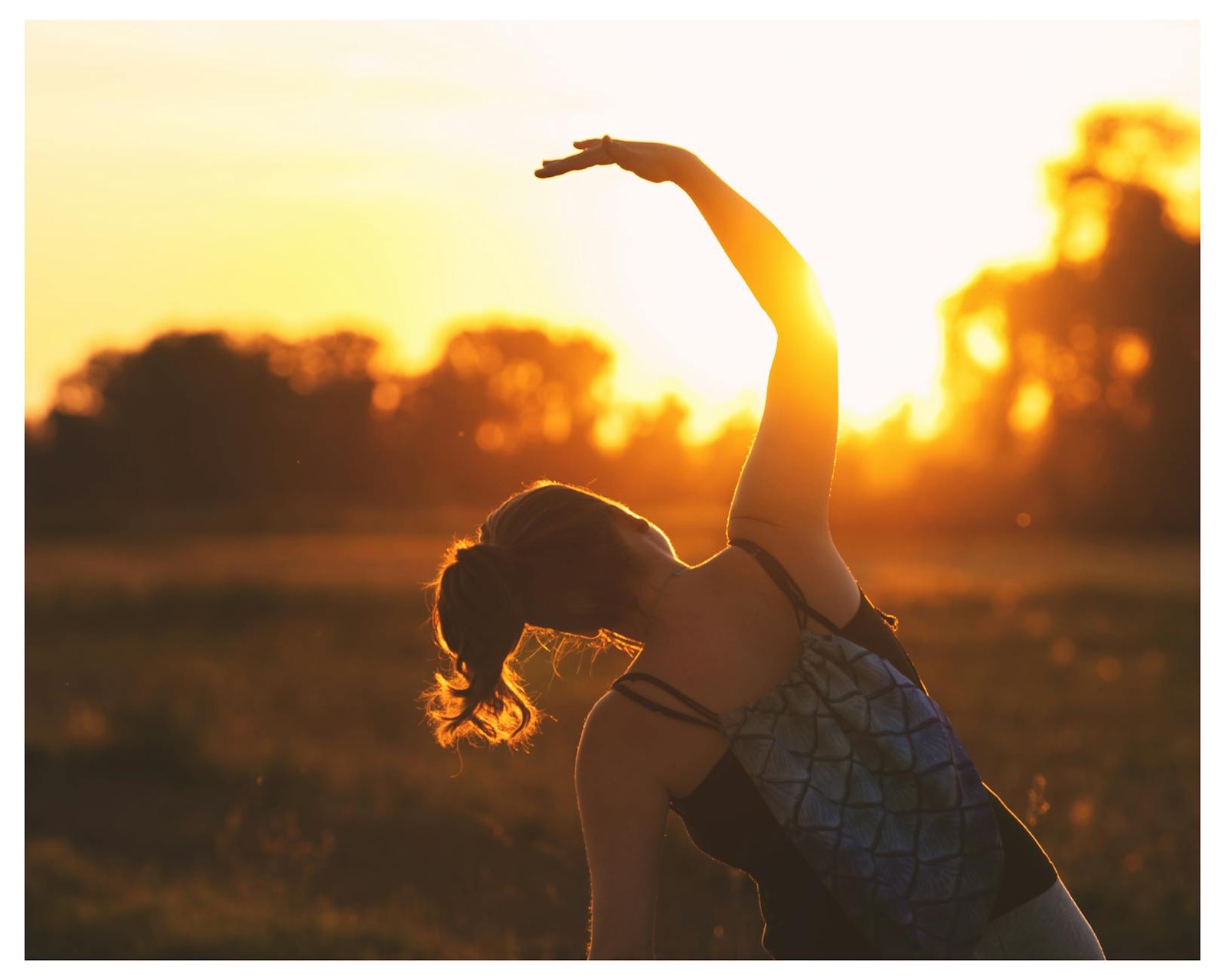 A woman stretching gently outdoors at golden sunrise
